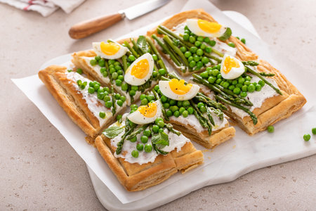 Fresh spring tart with green peas, boiled eggs and asparagus on puff pastry cut into piecesの写真素材