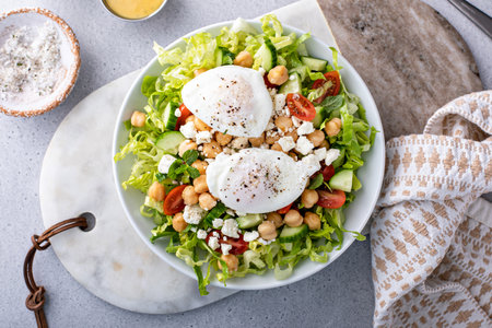 Fresh vegetable salad with chickpeas and feta cheese topped with poached egg, breakfast ideaの写真素材