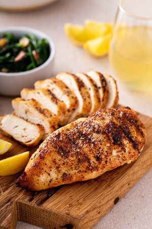 Grilled chicken breast with spice rub and lemon on a cutting board, sliced and wholeの写真素材