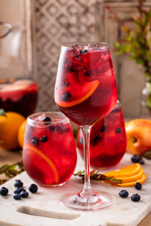 Refreshing summer berry sangria with apples, oranges and blueberry in wine glasses with iceの写真素材