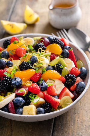 Fruit salad on a wooden table with berries and honey dressingの写真素材