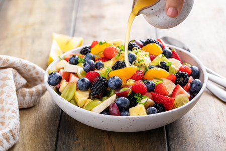 Fruit salad on a wooden table with berries and honey dressingの写真素材