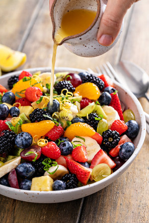 Fruit salad on a wooden table with berries and honey dressingの写真素材