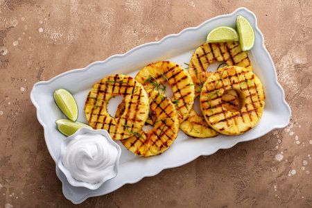 Grilled pineapple with lime honey glaze, lime zest and whipped cream on a serving plate overheadの写真素材
