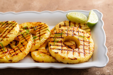 Grilled pineapple with lime honey glaze, lime zest and whipped cream on a serving plateの写真素材