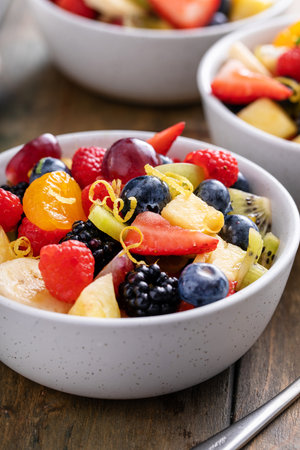 Fruit salad on a wooden table with berries, citrus zest, mint and honey dressing in small bowlsの写真素材