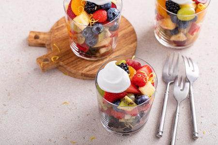 Fruit salad with berries, citrus zest, mint and honey dressing served in a glass with a dollop of whipped creamの写真素材