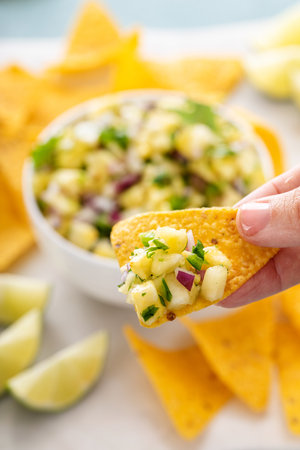 Fresh pineapple, red onion and jalapeno salsa in a bowl with tortilla chips being scooped with a chipの写真素材