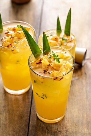 Grilled pineapple cocktail or mocktail in tall glasses garnished with pineapple leaves, refreshing summer drink ideaの写真素材