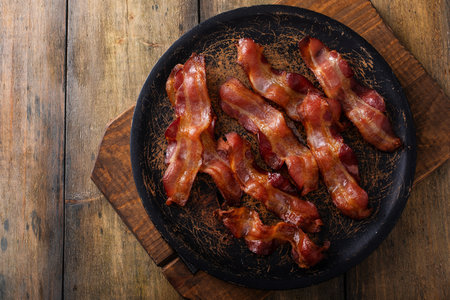 Cooked bacon on a wooden serving plate, ready to eat breakfast stapleの写真素材
