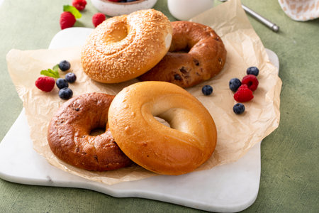Homemade freshly baked bagels on a parchment paper ready to eat, cinnamon raisin, sesame and plain bagel served with cream cheese and fresh berriesの写真素材