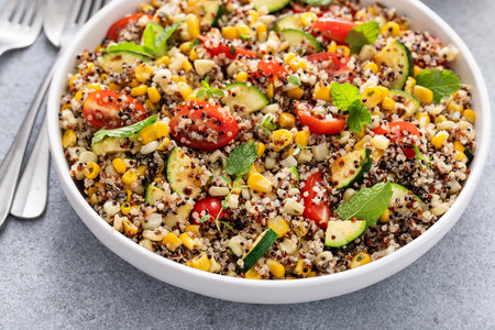 Warm quinoa salad with tomatoes, corn and zucchini with fresh mint and herbsの写真素材