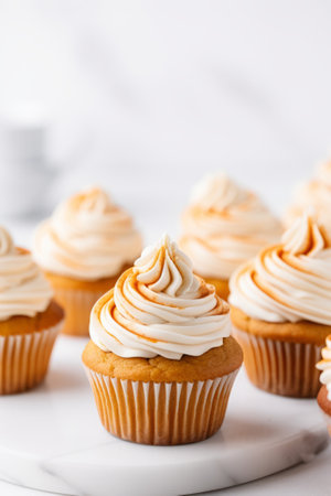 Pumpkin cupcakes on a white table topped with cream cheese frosting and cinnamon, generative AIの素材