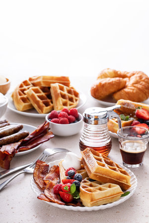 Breakfast table with waffles, bacon, breakfast sausage, croissants and fresh berriesの写真素材