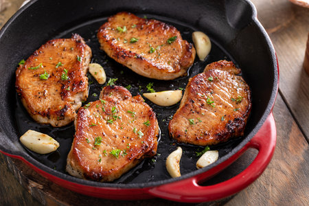 Pork chops seared in a cast iron pan with garlic and herbsの写真素材
