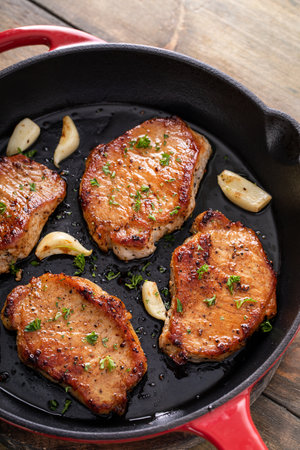 Pork chops seared in a cast iron pan with garlic and herbsの写真素材