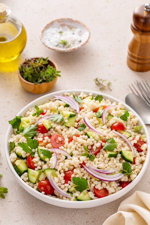 Pearl couscous salad with fresh vegetables and herbs in a serving bowl, healthy side dish ideaの写真素材