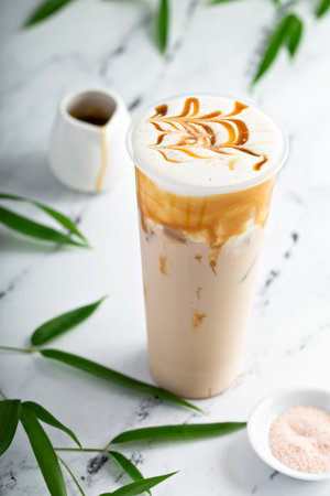 Caramel milk tea latte in a tall glass with cold foam and drizzled with caramel sauceの写真素材