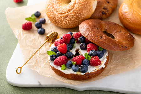 Cinnamon bagel with cream cheese, fresh berries and honey for breakfastの写真素材