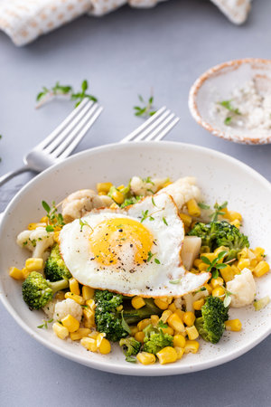 Healthy breakfast or lunch with cauliflower, broccoli and corn topped with fried eggの写真素材