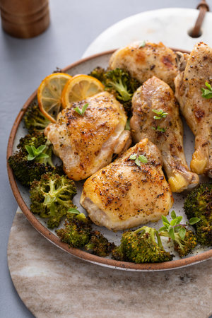 Chicken drumsticks and thighs with broccoli roasted on a serving plate for dinner or lunch with garlic and herbsの写真素材