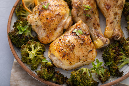 Chicken drumsticks and thighs with broccoli roasted on a serving plate for dinner or lunch with garlic and herbsの写真素材