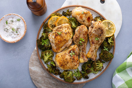 Chicken drumsticks and thighs with broccoli roasted on a serving plate for dinner or lunch with garlic and herbsの写真素材