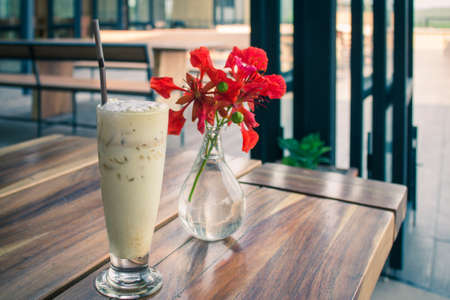 Latte Coffee And red flowers are in the glass, vases laid on wooden boards.の写真素材