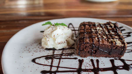 Brownies topped with chocolate and whipped cream. In a white plate on a wooden table.の写真素材