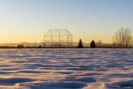 Evening winter Coloradan landscape with baseball backstop, trees and the Rocky Mountains in the distanceの写真素材