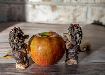 Big red apple and funny trolls figures on the wooden table against the brick wallの写真素材