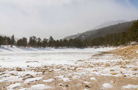 A beautiful view of the tall trees and a frozen lake near Allenspark, Colorado. Rocky mountains in...