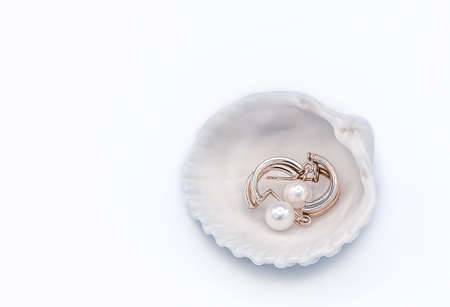 Pair of golden earrings with pearls lying inside of the sea shell on a white backgroundの写真素材