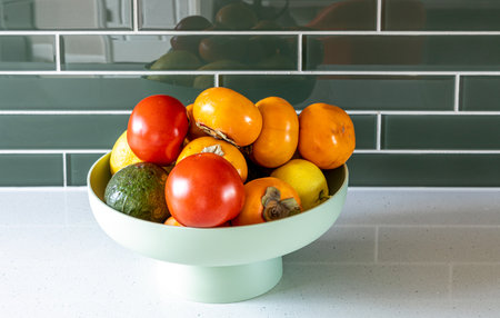 Avocado, tomato, persimmons, and lemons in the green plastic vase on the kitchen countertop