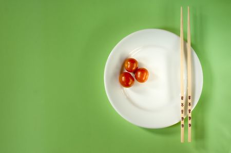 Three cherry tomatoes on a white plate with chopsticks