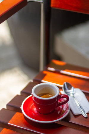 small red cup espresso with stainless steel spoon and paper tissue in the wooden chair at outdoorの写真素材