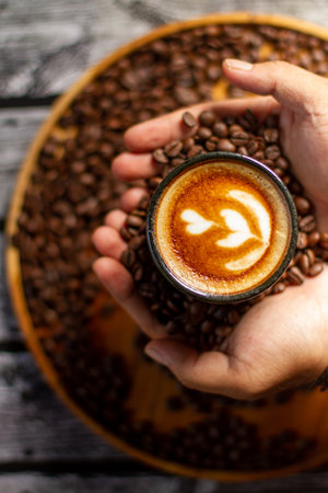 Male hand with cup of coffee latte art with blurred coffee roasted backgroundの写真素材