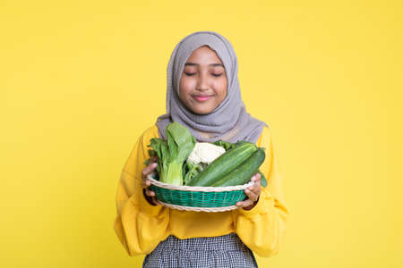 Happy asian woman holding straw basket with healthy vegetables on yellow background.の写真素材