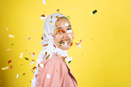 Beautiful young woman throwing confetti and looking happy on yellow backgroundの写真素材