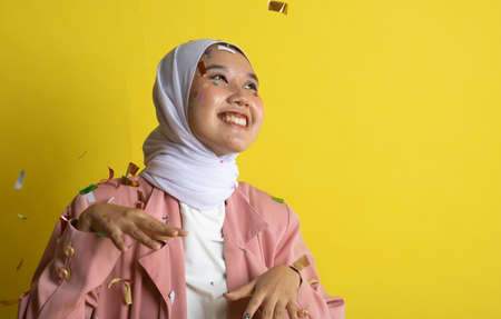 Beautiful young woman throwing confetti and looking happy on yellow backgroundの写真素材