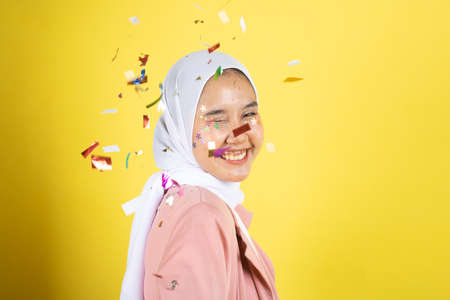 Beautiful young woman throwing confetti and looking happy on yellow background