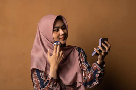 Portrait of beautiful asian woman applying powder puff at cheek makeup of cosmetic isolated on gold background.の写真素材