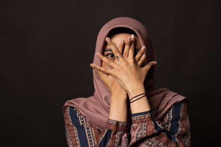 Asian woman covering her face with both hands on black background.の写真素材