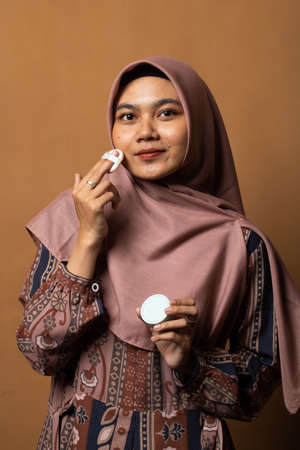 Portrait of beautiful asian woman applying powder puff at cheek makeup of cosmetic isolated on gold background.の写真素材