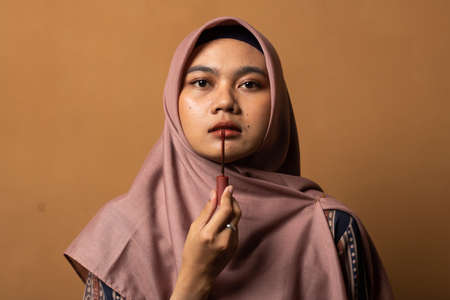 Asian young woman showing skincare products on gold background.