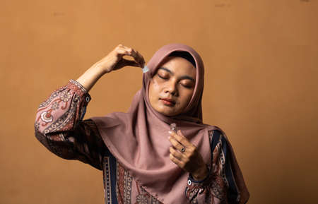 Asian young woman showing skincare products on gold background.