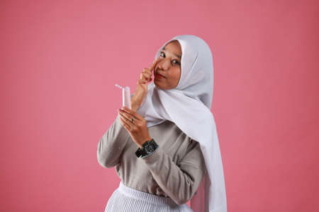 Asian young woman showing skincare products on pink background.