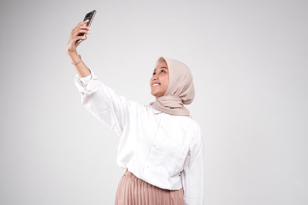 Hijab woman taking selfie with mobile phone isolated on white background.の写真素材