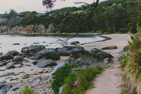 deserted beach in Hobart, Tasmania with rocks and walkpath in the foreground on an overcast day with slightly muted tonesの写真素材