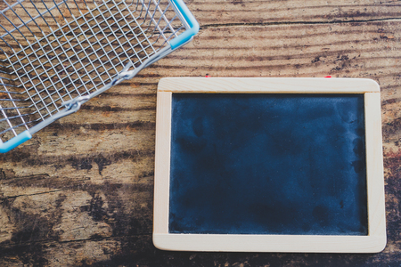 blackboard next to empty shopping cart with copyspace to add your text, on wooden tableの写真素材